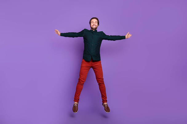 Photo of charming excited young guy dressed smart casual clothes jumping high smiling isolated violet color background. - Фото, зображення