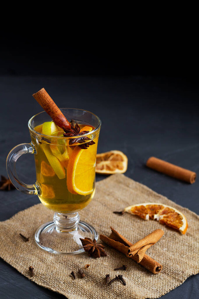 Seasonal mulled drink with copy space. Christmas hot white mulled wine in glass with orange, honey, cinnamon sticks and star anise with spices and ingredients on black background. Spicy warm beverage. - Photo, Image