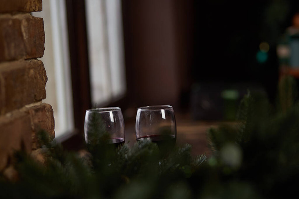 Weingläser in heimischer Weihnachtsatmosphäre auf der Fensterbank. Verschwommener Vordergrund. Kopierraum. Unauffällige Festkarte oder Hintergrund. Hochwertiges Foto - Foto, Bild