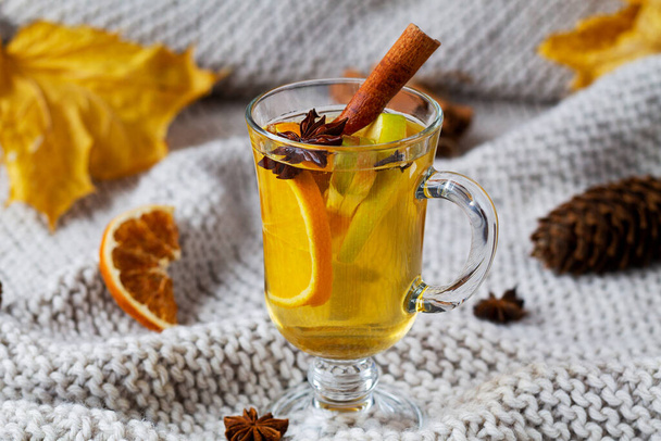 mulled wine with spices.Mulled drink on knitting plaid with copy space. Christmas hot white mulled wine in glass with orange, honey, cinnamon sticks and star anise dry leaves on light background. - Fotó, kép