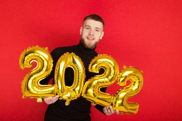 Retrato de un hombre con los números 2022 sobre un fondo rojo. El próximo Año Nuevo - Foto, imagen
