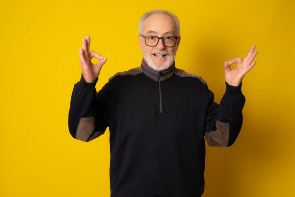 Amazed mature man wearing winter clothing with okay sign isolated over yellow background. - Фото, изображение