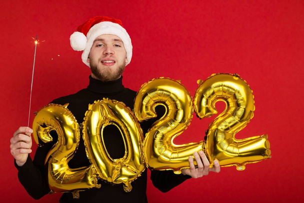 A man in a Santa Claus hat holds the numbers 2022 and a sparkler - Photo, Image