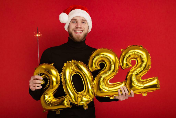 Ein Mann mit Nikolausmütze hält die Zahlen 2022 und eine Wunderkerze in der Hand. - Foto, Bild