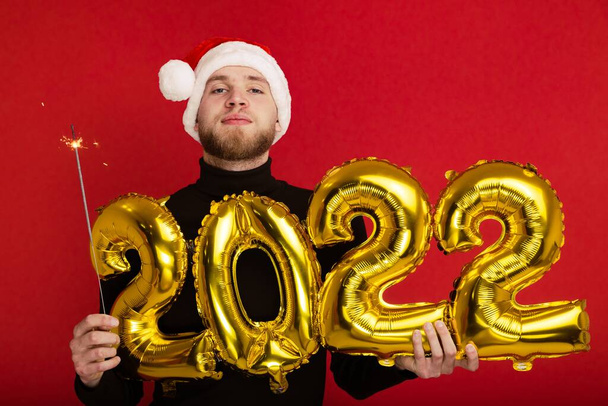 Człowiek w czapce Świętego Mikołaja trzyma numery 2022 i blask - Zdjęcie, obraz