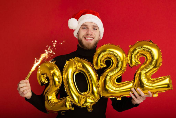 Un hombre con un sombrero de Santa Claus sostiene los números 2022 y un chispeante - Foto, Imagen