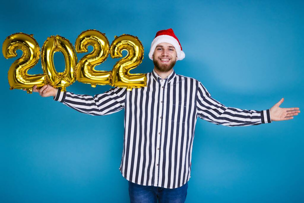 Um homem em um chapéu de Natal segura os números 2022 de balões infláveis - Foto, Imagem