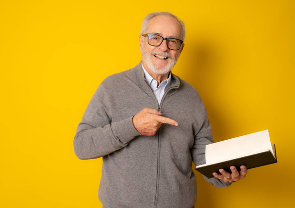 Mature smiling man reading a book isolated over yellow background. - Foto, immagini