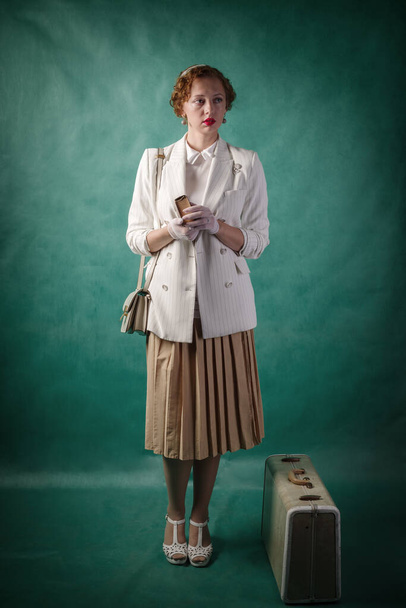 Young woman, dressed in retro style, with a suitcase and a book in her hands. Studio portrait - Fotografie, Obrázek