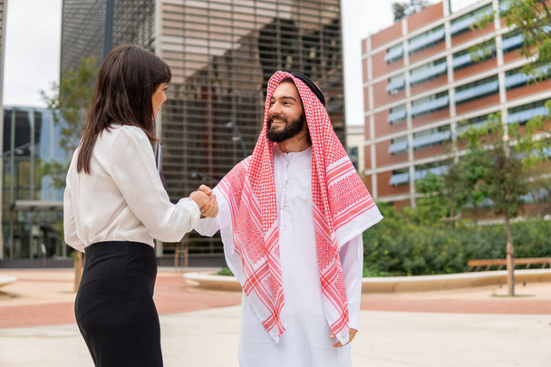 Lächelnder arabischer Mann und kaukasische Geschäftsfrau beim Händeschütteln nach Vertragsunterzeichnung im Freien - Foto, Bild