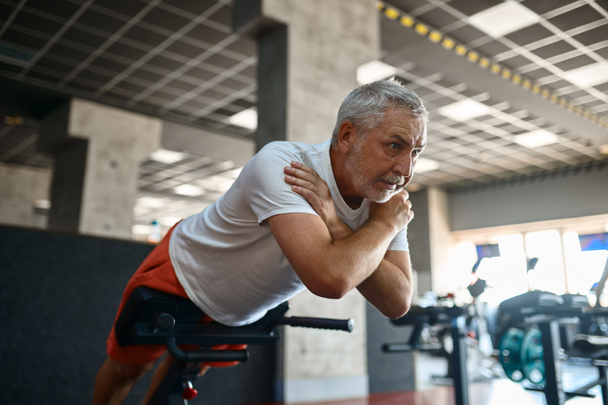 Starší muž ve sportovním oblečení dělá břišní cvičení, tělocvična - Fotografie, Obrázek
