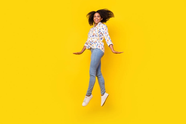Full body profile photo of cute millennial curly hairdo lady jump wear blouse jeans sneakers isolated on yellow background - Foto, imagen