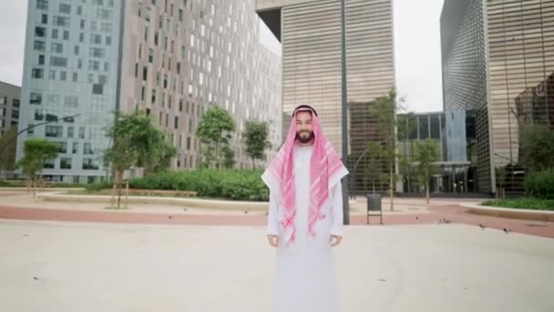 Zoom szczęśliwego uśmiechniętego arabczyka stojącego na ulicy miasta, patrzącego w kamerę - Materiał filmowy, wideo