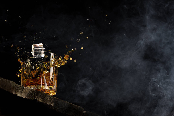 whiskey in een glas op een zwarte achtergrond op een houten tafel - Foto, afbeelding