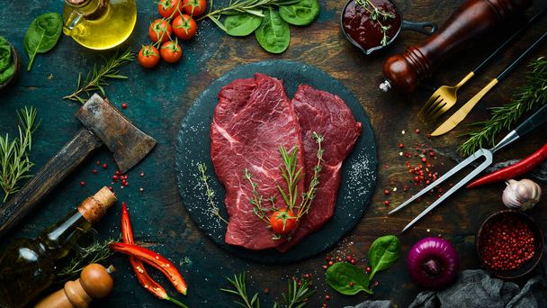 Meat. Raw veal steak with rosemary and spices. On a black stone background. Top view. - Фото, зображення