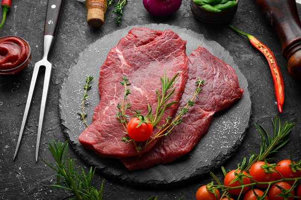 Meat. Raw veal steak with rosemary and spices. On a black stone background. Top view. - Foto, Imagem