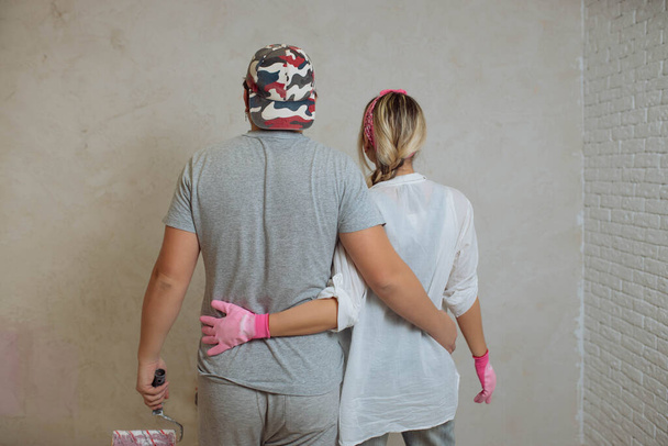 Een gelukkig jong gezin maakt met eigen handen een droomreparatie in het huis. Man en vrouw schilderen de muur in de kamer - Foto, afbeelding