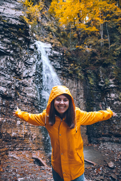 portrét ženy ve žlutém plášti před podzimním pojetím vodopádu - Fotografie, Obrázek