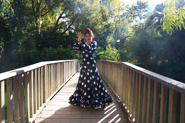 piękna hiszpańska brunetka tancerka flamenco w typowym stroju flamenco z białymi kropkami polki tańczącymi na drewnianym wybiegu na ulicy. Flamenco dziedzictwo kulturowe ludzkości. - Zdjęcie, obraz