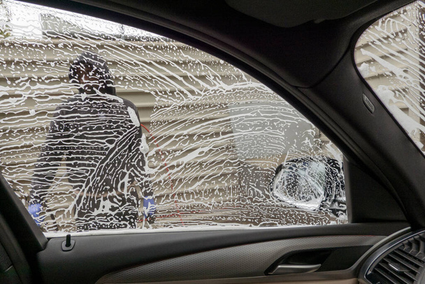 Winchester, Hampshire, Verenigd Koninkrijk. 2021. Drivers eye view van carwash medewerker, zeep peulen en water tijdens een carwash - Foto, afbeelding