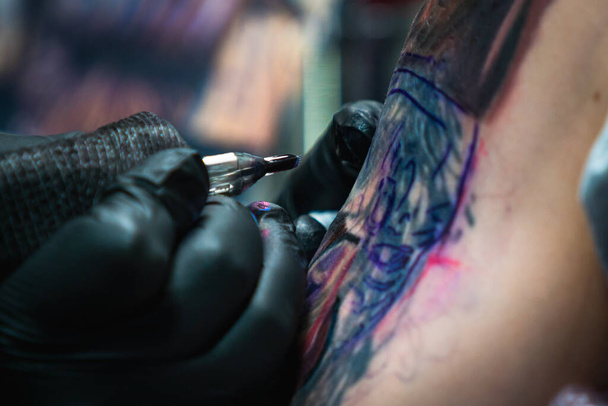Artista profesional del tatuaje hace un tatuaje en una mano de hombre joven, primer plano - Foto, Imagen