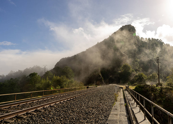 Eisenbahnlinie, die direkt zu einem Tunnel führt, der den Berg überquert und Nebel im Mund hat - Foto, Bild