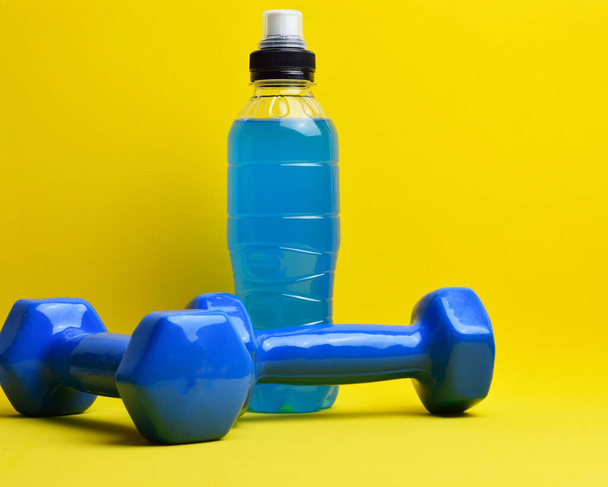 Dumbells and bottle of isotonic drink on yellow background. - Foto, imagen