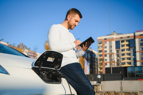 Handsome young man watching his car charging - Foto, Imagem