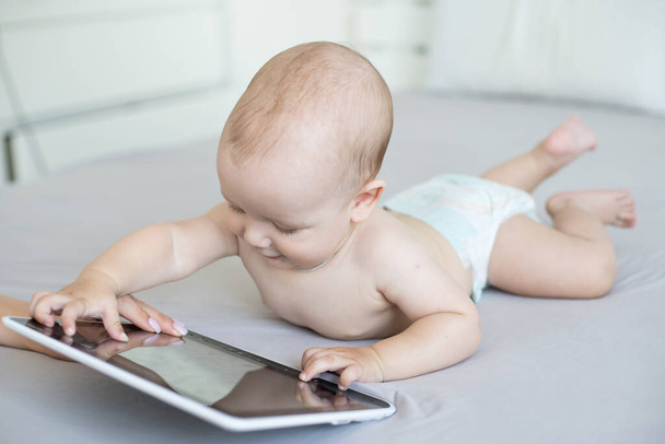 A six-month baby with a tablet computer, looking at screen, at home - Foto, immagini