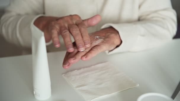 Γριά γυναίκα με ρυτίδες βάζει ενυδατική κρέμα στα χέρια - Πλάνα, βίντεο