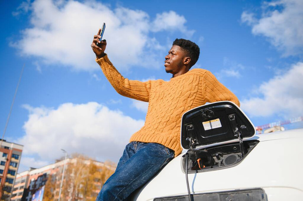 African American man charging his electric car. - 写真・画像