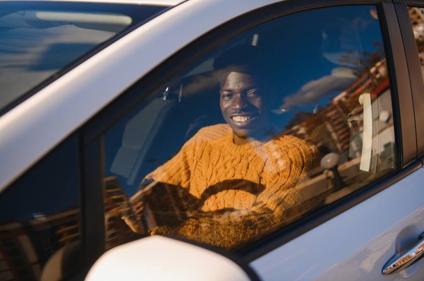 Handsome young African American man in his new high-tech electric vehicle while drinking. Self driving vehicle concept - Foto, imagen