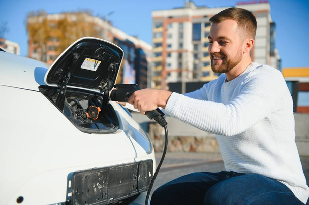young handsome man holding charging cable at electric charging station point standing near his new car. - Φωτογραφία, εικόνα