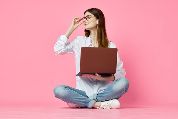 cheerful woman with laptop sitting on the floor on a pink background - Foto, Imagem