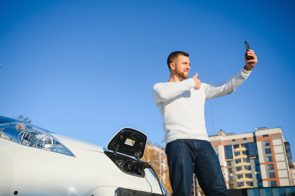 Человек заряжает электромобиль на зарядной станции - Фото, изображение