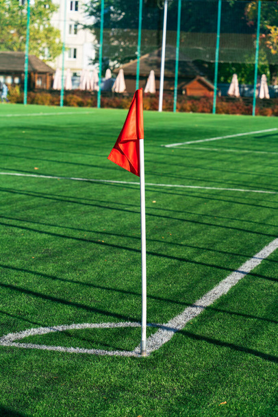 Red flag on the border of a green soccer field, long shadows of the fencing mesh in the rays of the evening sun - Fotó, kép