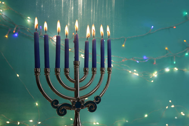Image of jewish holiday Hanukkah with menorah (traditional candelabra) and candles over garland glitter lights background - Zdjęcie, obraz
