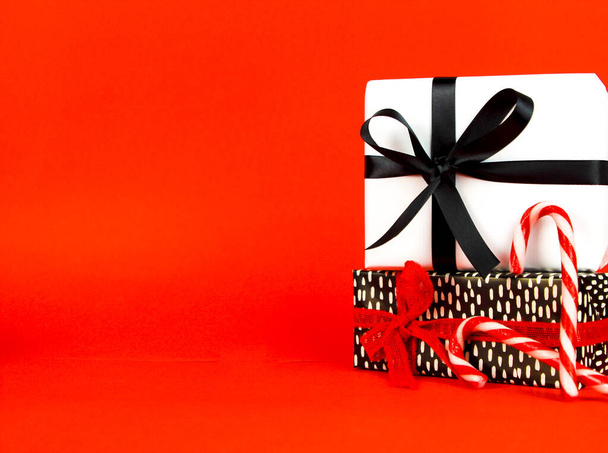 Cadeaus verpakt met zwart-wit papier en rode en zwarte strikken naast kerstversiering op rode achtergrond - Foto, afbeelding
