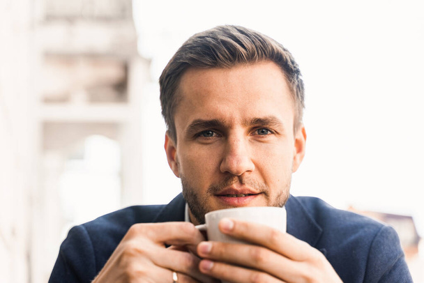 Man like coffee. Handsome man with cup of coffee in cafe. Morning lifestyle of male. Man is sitting on the summer terrace in cafe, drinking coffee and smiling - Фото, изображение