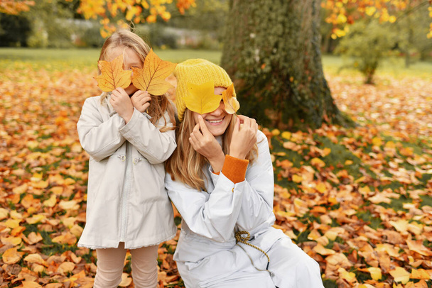 Little girl and her mother playing in the autumn park - Фото, изображение
