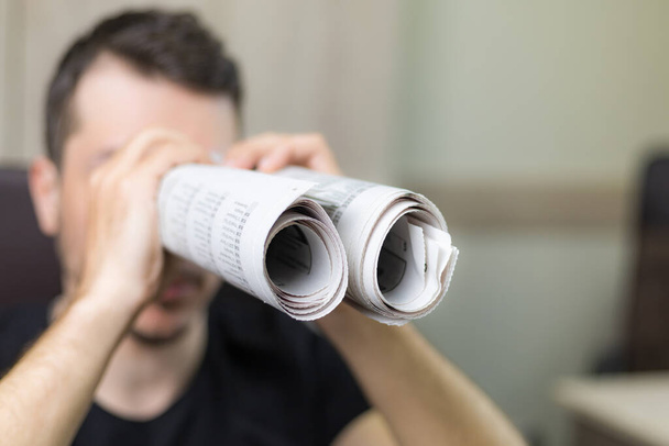 Man holding two twisted roll newspaper. Metaphor or allegory with binoculars. Selective focus on newspapers. Truth search concept - Φωτογραφία, εικόνα