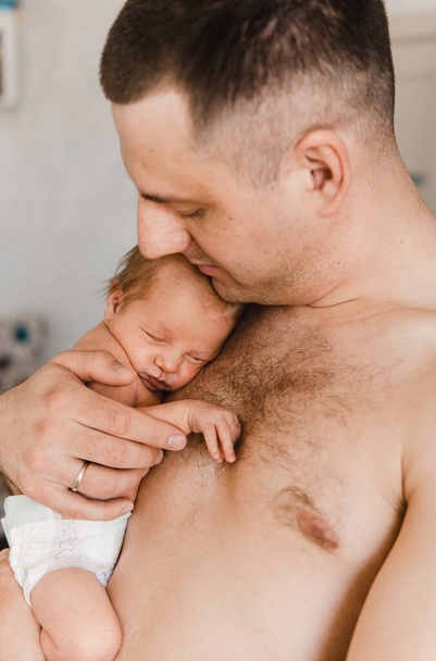 Portrait of father holding sleeping newborn son on his arm. Newborn baby in diaper in fathers hands. Selective focus. Film grain - Fotografie, Obrázek