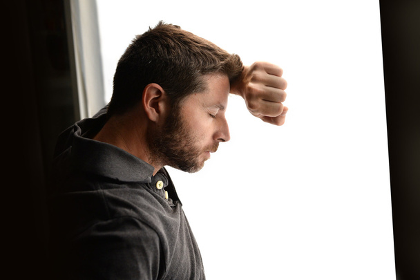 Hombre atractivo apoyado en la ventana sufriendo crisis emocionales y depresión
 - Foto, imagen
