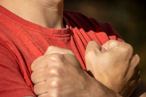 Mężczyzna w czerwonej koszulce skrzyżował ręce nad klatką piersiową. - Zdjęcie, obraz