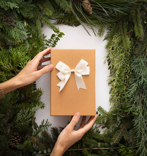 Homemade white copyspace and conifer brunches and cones in corners beautifuly arranged flat lay do it yourself minimalism natural art with recyclable packaging gift with bow hands hold - Fotó, kép