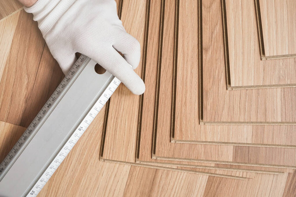 Installing laminated floor, detail on hand in white gloves holding steel ruler over wooden tiles - Fotografie, Obrázek