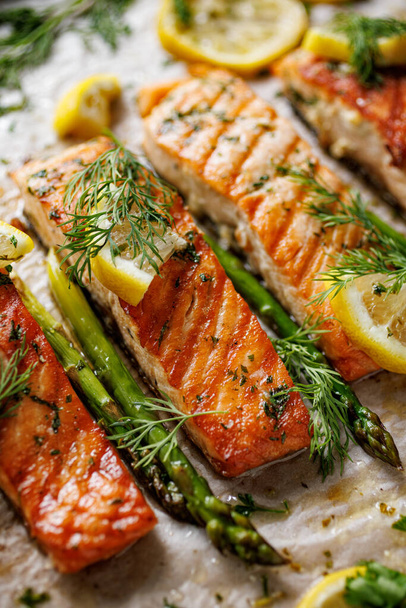 Baked salmon fillets and green asparagus with aromatic herbs and lemon on baking paper, focus on the portion inside, close-up - Photo, Image