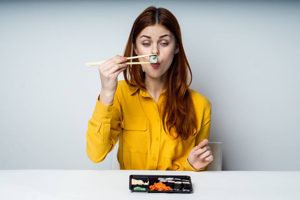 a woman in a yellow shirt sits at a table and eats sushi - Фото, зображення