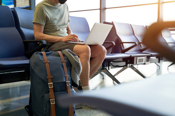 asiatico uomo maschio aria viaggiatore con nero faccia maschera seduta in attesa in aeroporto terminal edificio utilizzando computer portatile - Foto, immagini