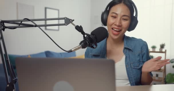 Happy asia girl record a podcast on laptop computer with headphones and microphone talk with audience at living room. Female podcaster make audio podcast from her home studio. Stay at house concept. - Footage, Video